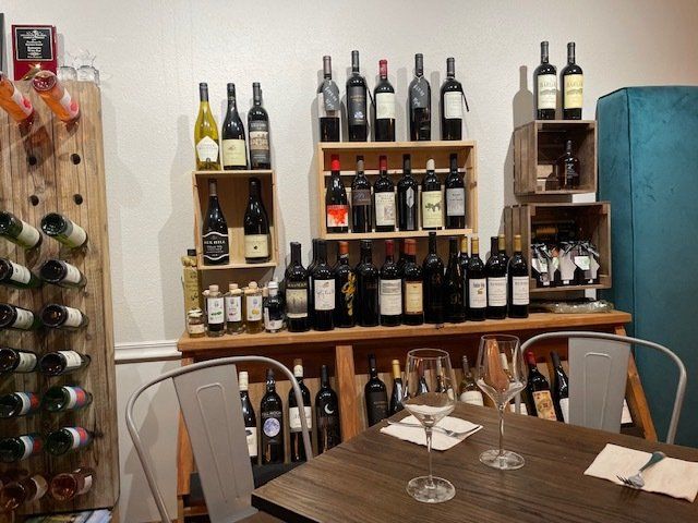 A table with a glass on it in front of a display of wine bottles.
