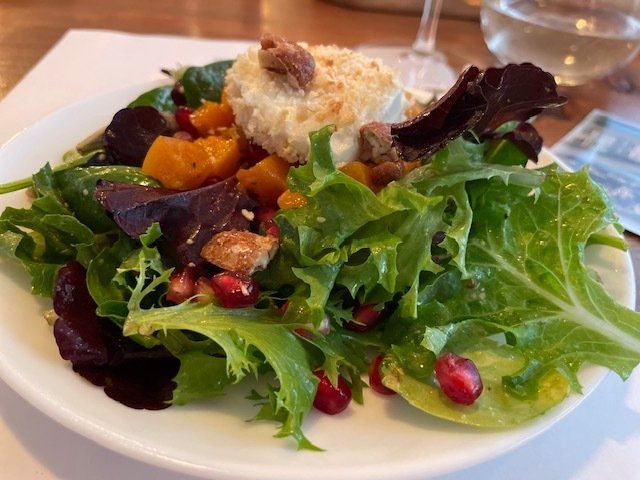 A salad with lettuce and pomegranate seeds on a white plate