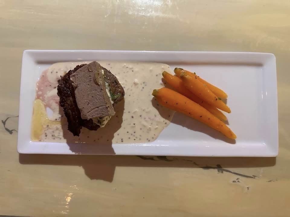 A white plate topped with meat and carrots on a table.