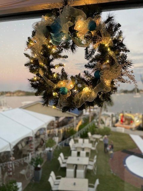 A christmas wreath is hanging from a window overlooking a lawn with tables and chairs.