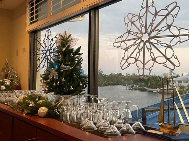 A christmas tree and wine glasses are on a counter in front of a window.