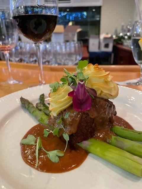 A close up of a plate of food with a glass of wine in the background