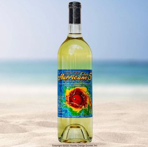 A bottle of blue champagne is sitting on a wooden table in front of purple flowers.
