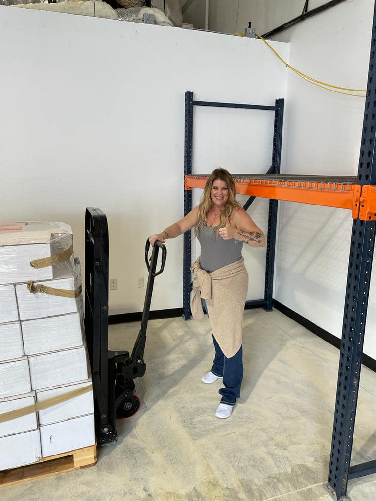 A woman is pushing a forklift in a warehouse.