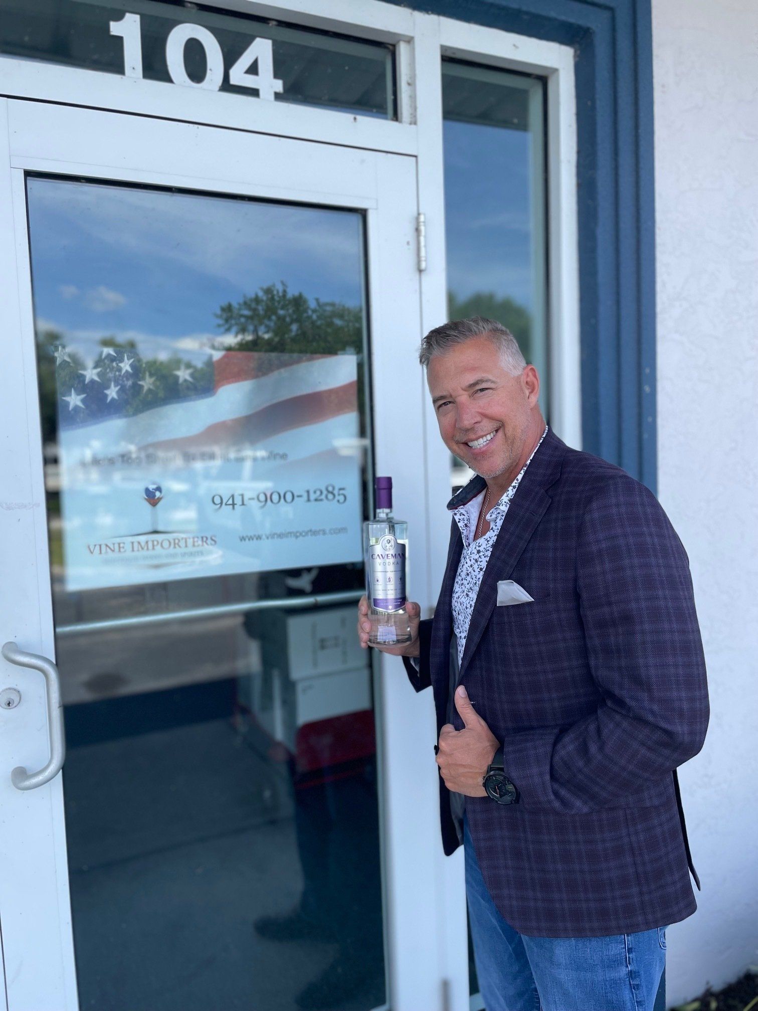 A man is standing in front of a door holding a bottle of vodka.