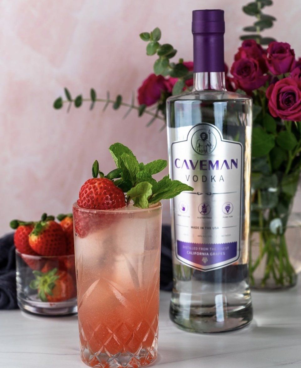 A bottle of caveman vodka next to a glass with strawberries in it