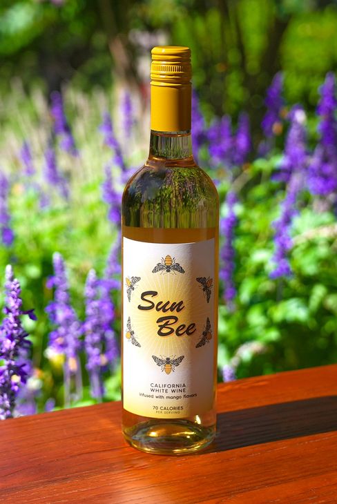 A bottle of blue champagne is sitting on a wooden table in front of purple flowers.