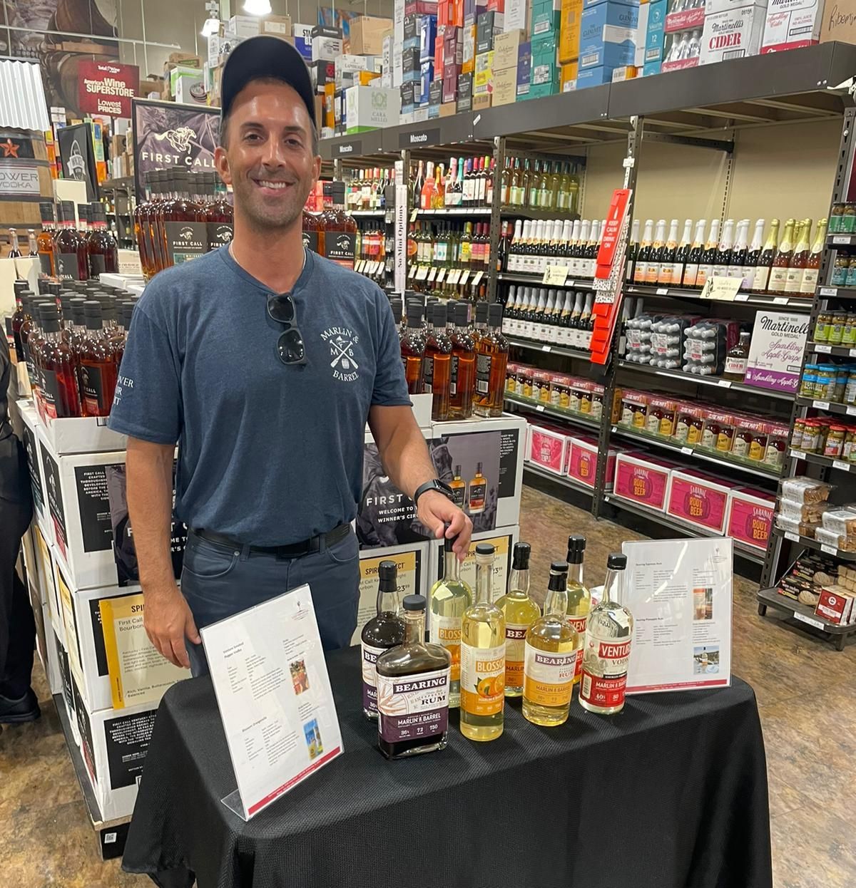 A man is standing in front of a table with bottles of alcohol on it.