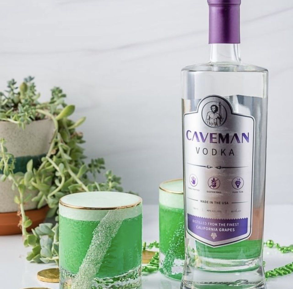 A bottle of caveman vodka next to two green glasses
