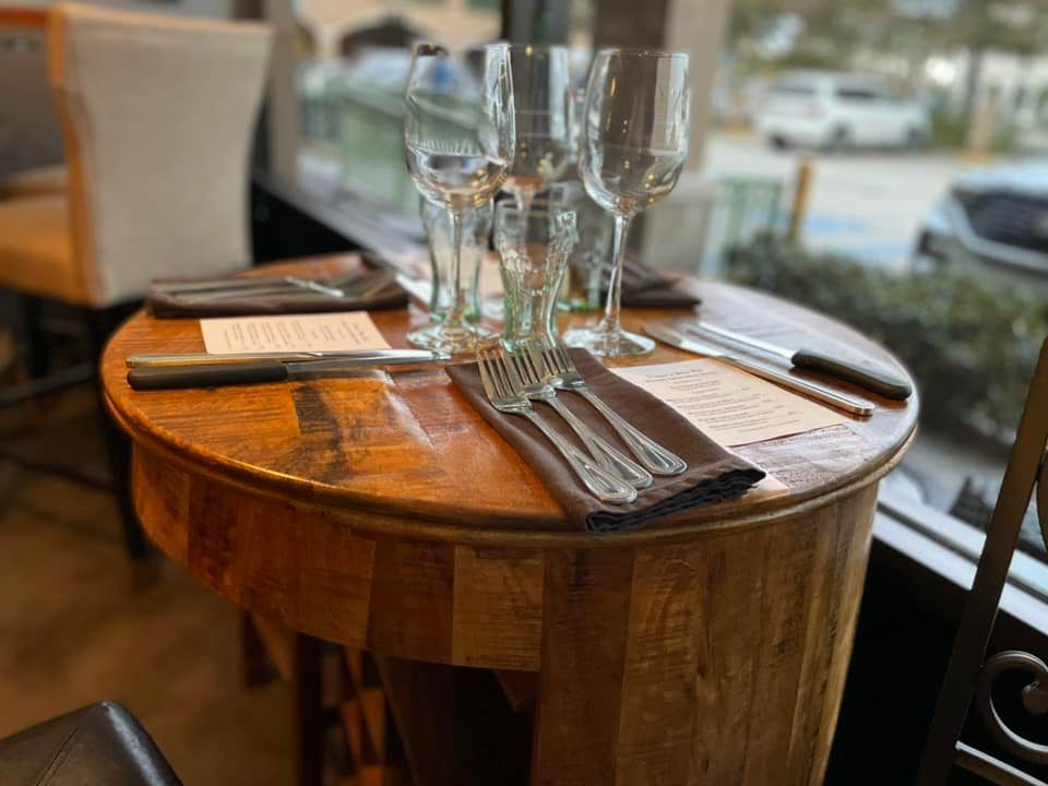 A wooden table with silverware and wine glasses on it in a restaurant.