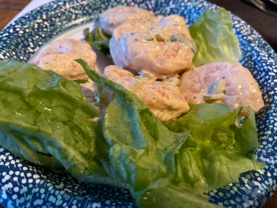 A plate of shrimp salad with lettuce on a paper plate.