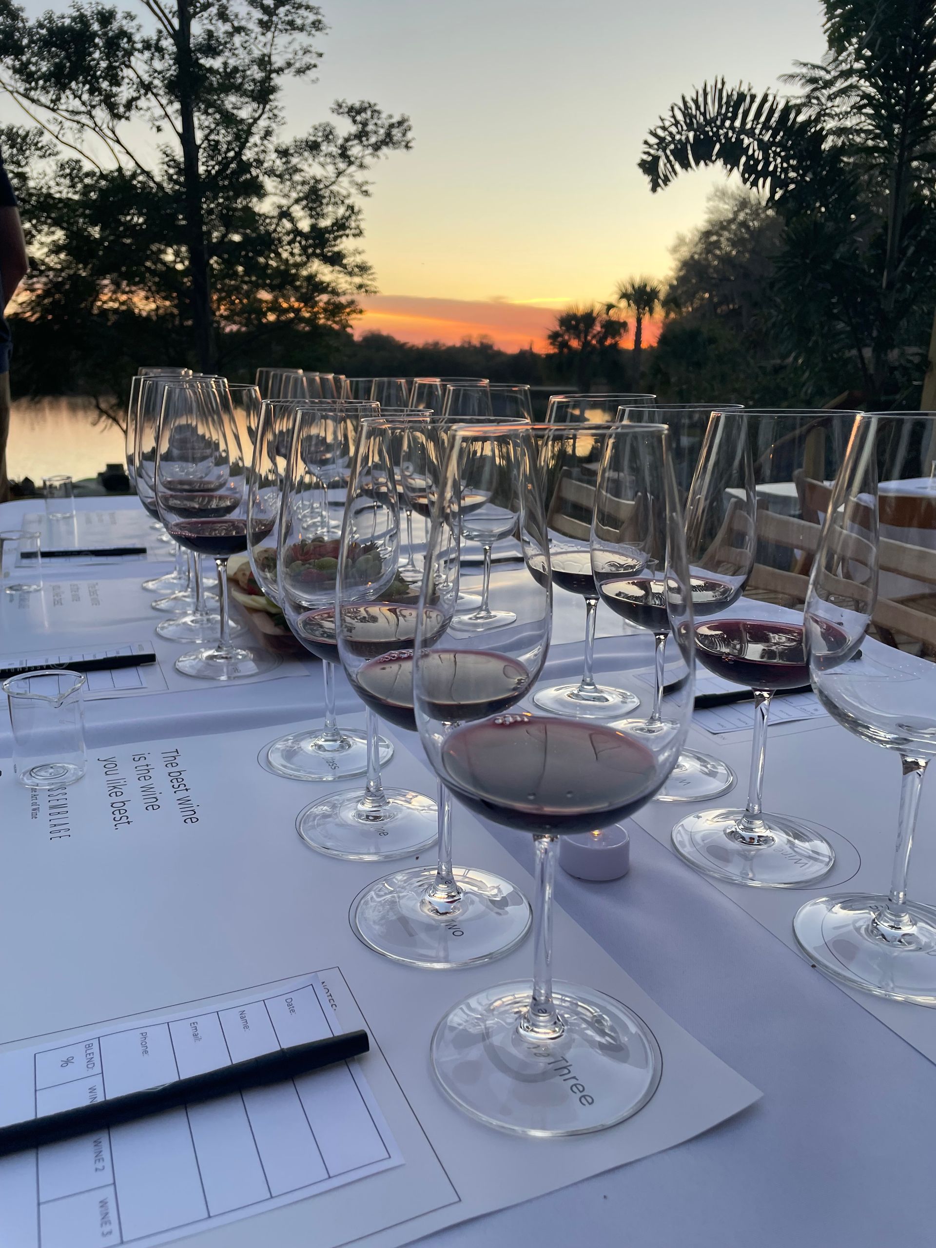 A row of wine glasses on a table with a sunset in the background.