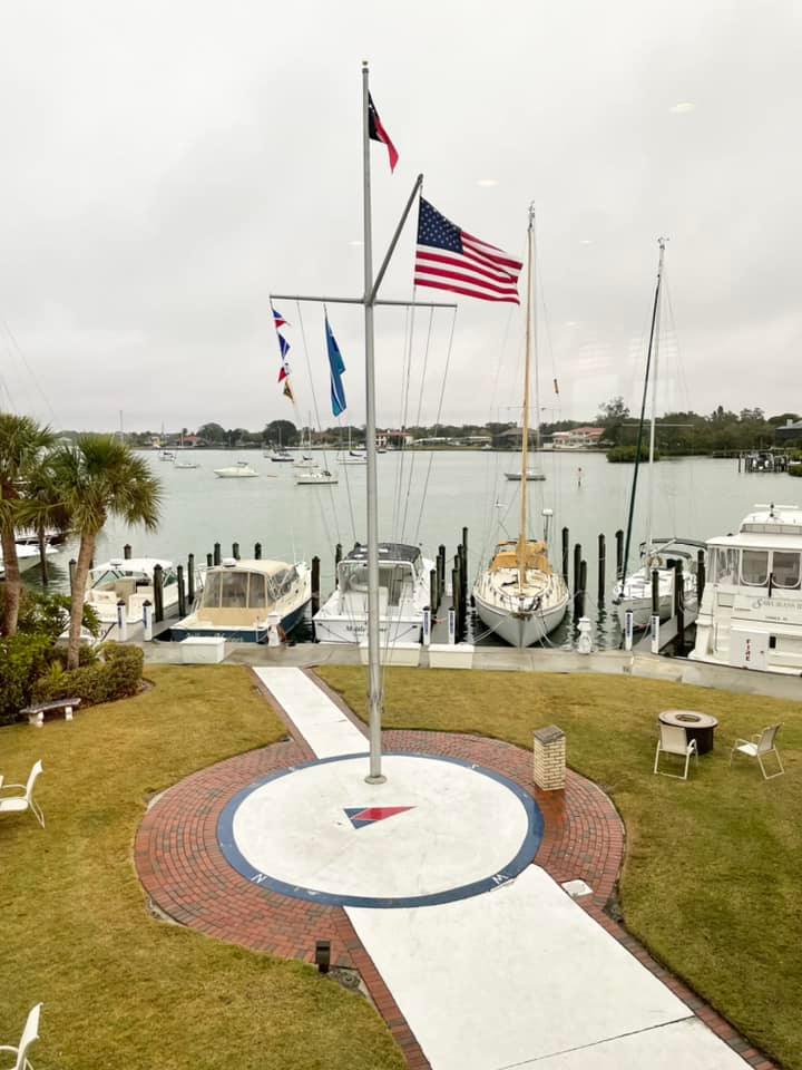 A group of boats are docked in a marina with an american flag flying in the foreground.