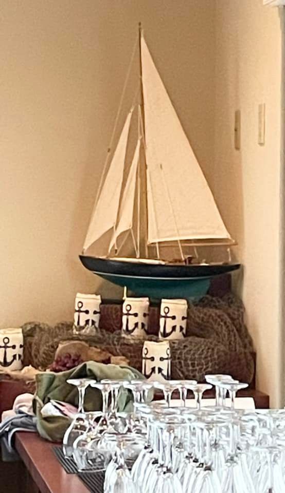 A model sailboat is sitting on top of a table next to wine glasses.