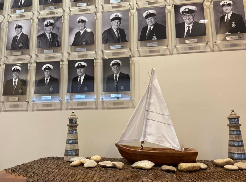 A model sailboat sits in front of a wall of captains