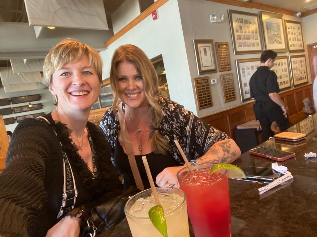 Two women are sitting at a table with drinks and smiling.
