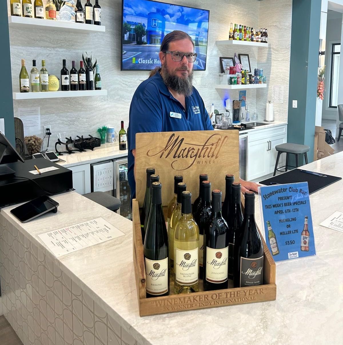 A man is standing behind a counter with a display of wine bottles.
