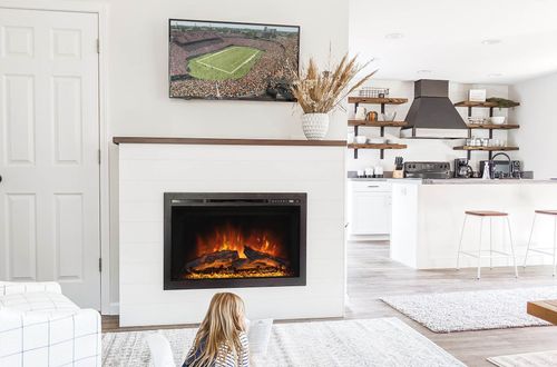 Cozy living room with a fireplace and TV; a child sits on the rug, facing the fireplace.