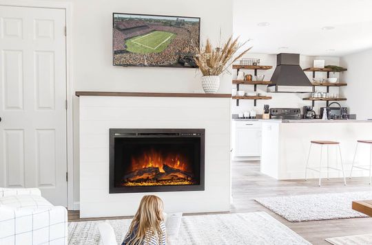 Cozy living room with a fireplace and TV; a child sits on the rug, facing the fireplace.