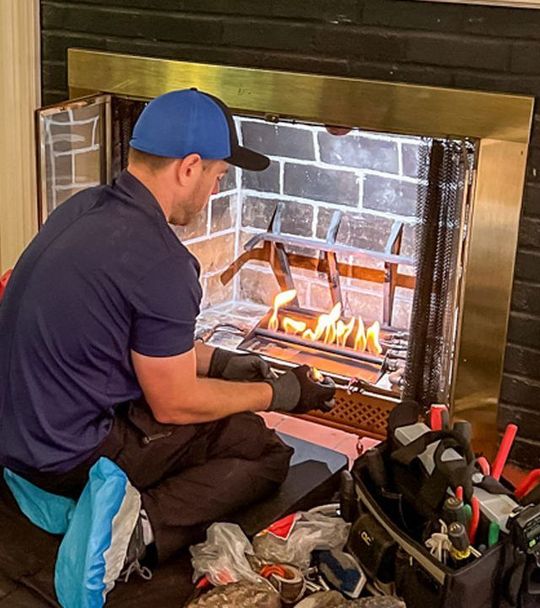A man in a blue cap and gloves inspecting a fireplace. Tools and debris sit in front.