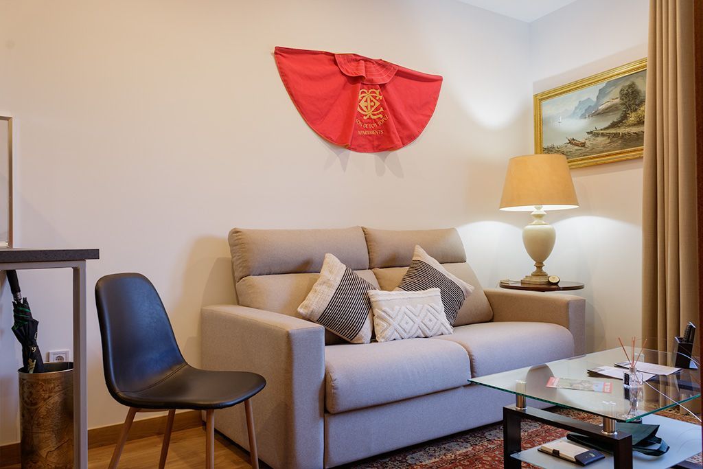 A living room with a couch , chair , lamp and a red matador cape on the wall.