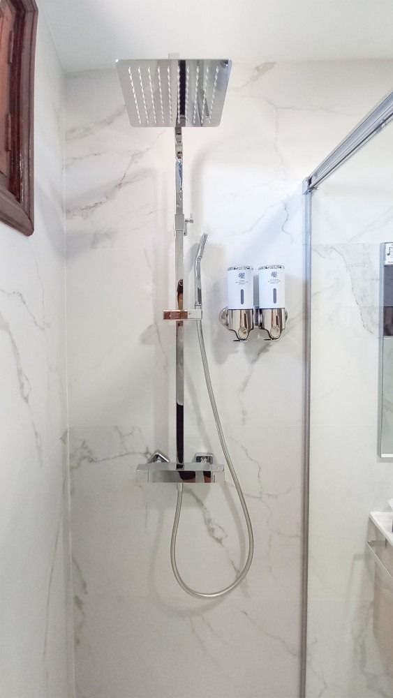 A bathroom with a shower head and soap dispensers on the wall.