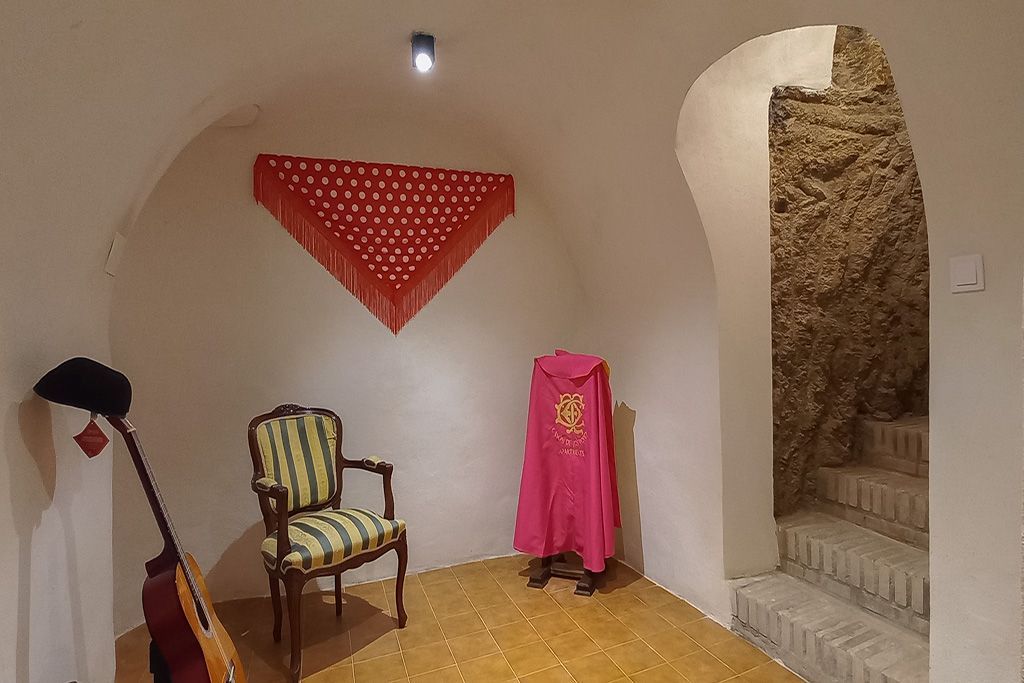 A room with a chair , guitar , shawl and stairs.