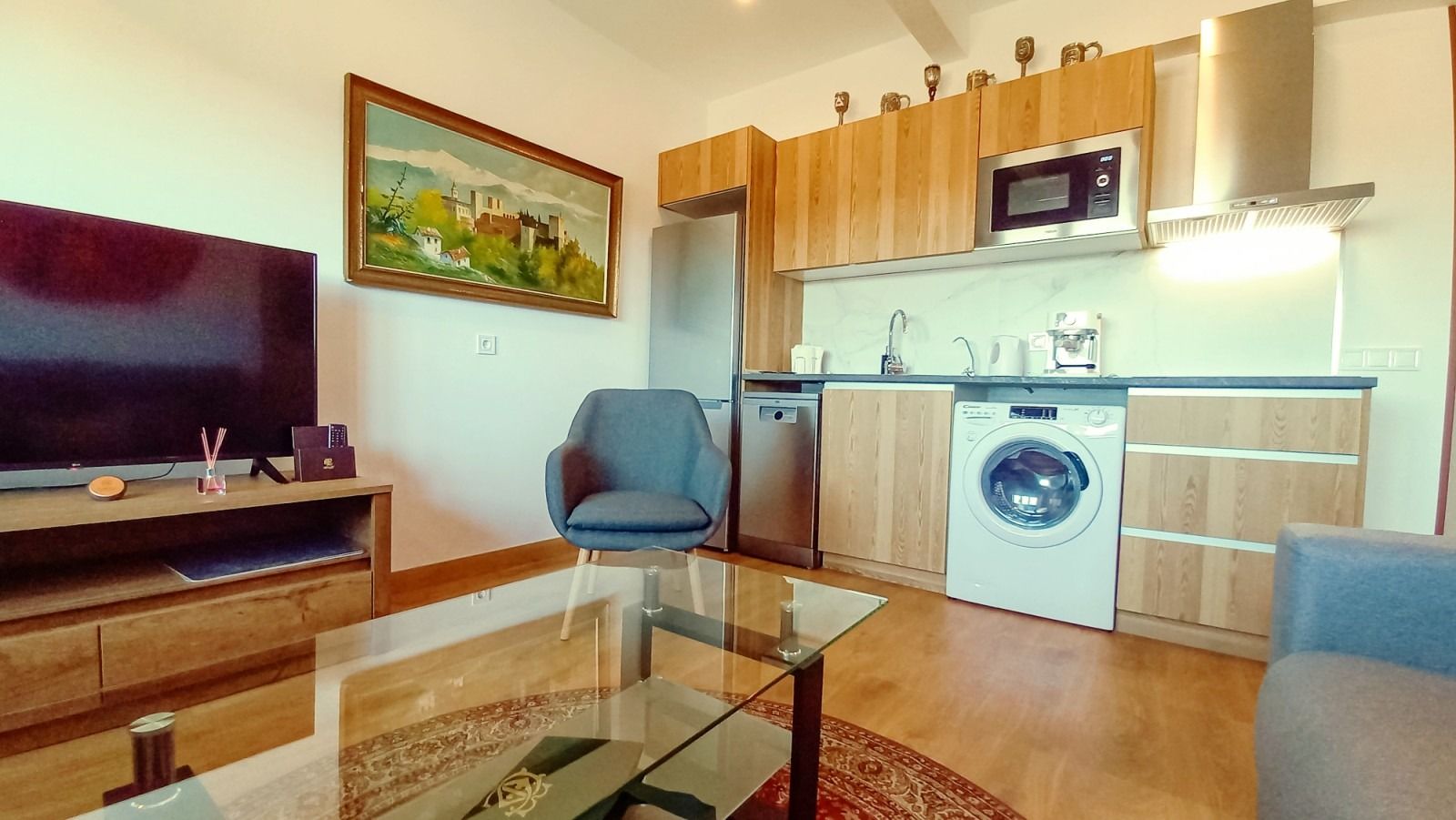 A living room with a couch , chair , television , washing machine and microwave.