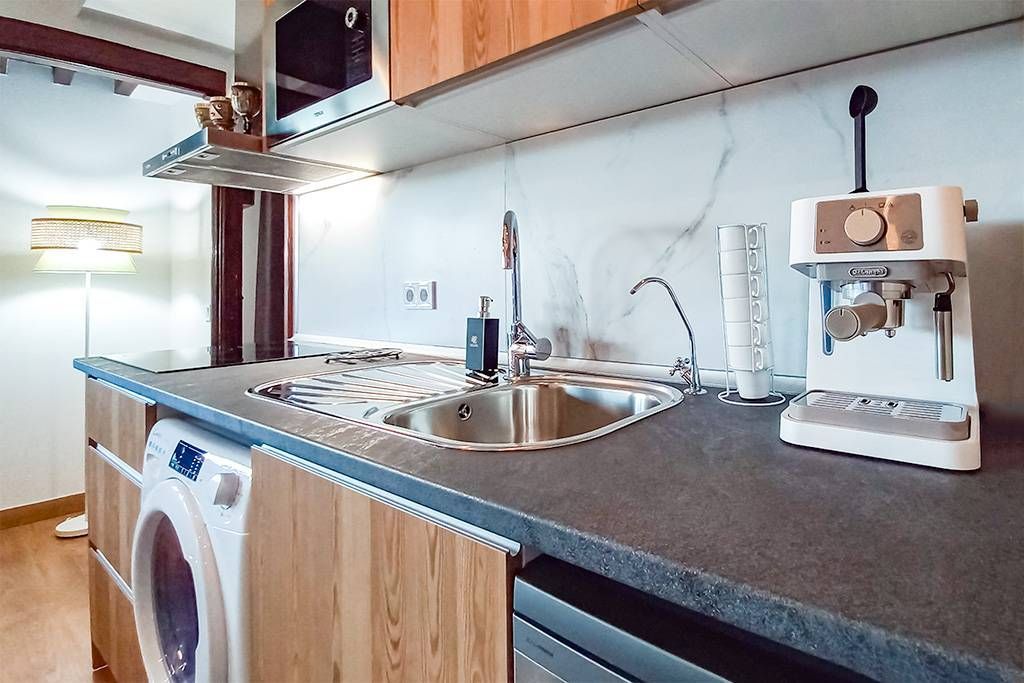 A kitchen with a sink , washer and dryer and a coffee maker on the counter.