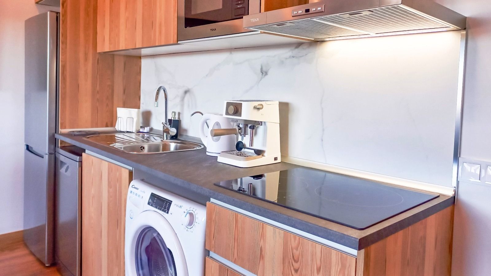 A kitchen with a washing machine , stove top oven , microwave and refrigerator.