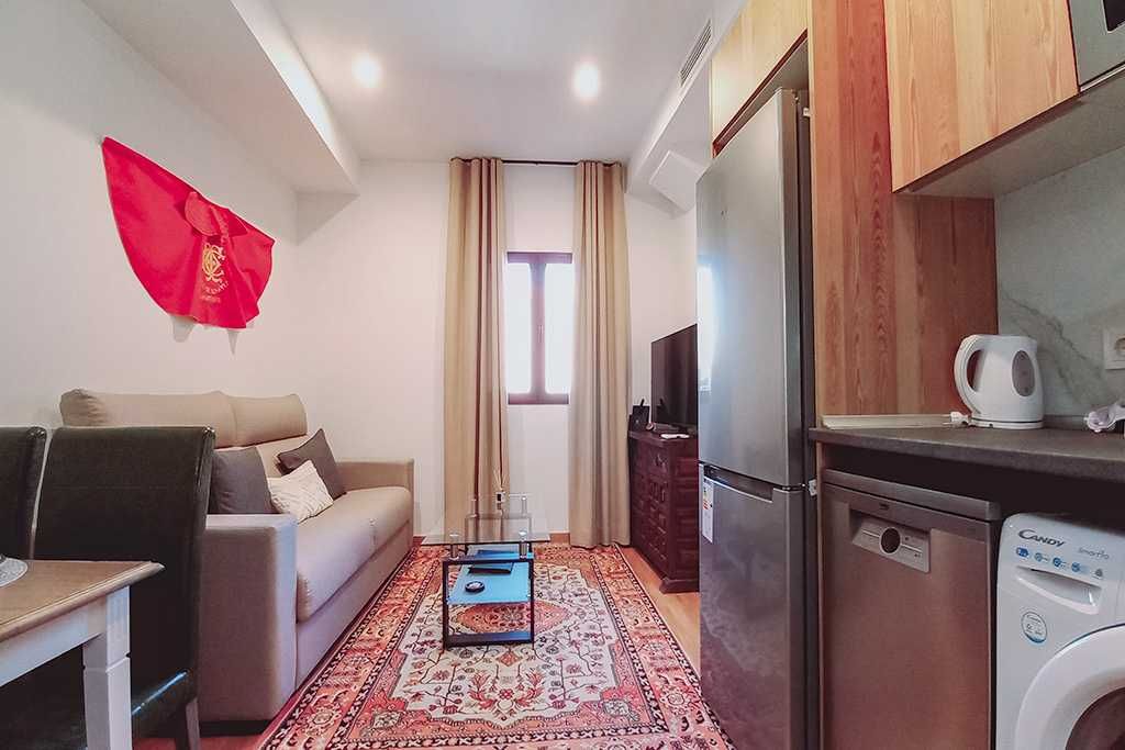 A living room with a couch , table , chairs and a refrigerator.