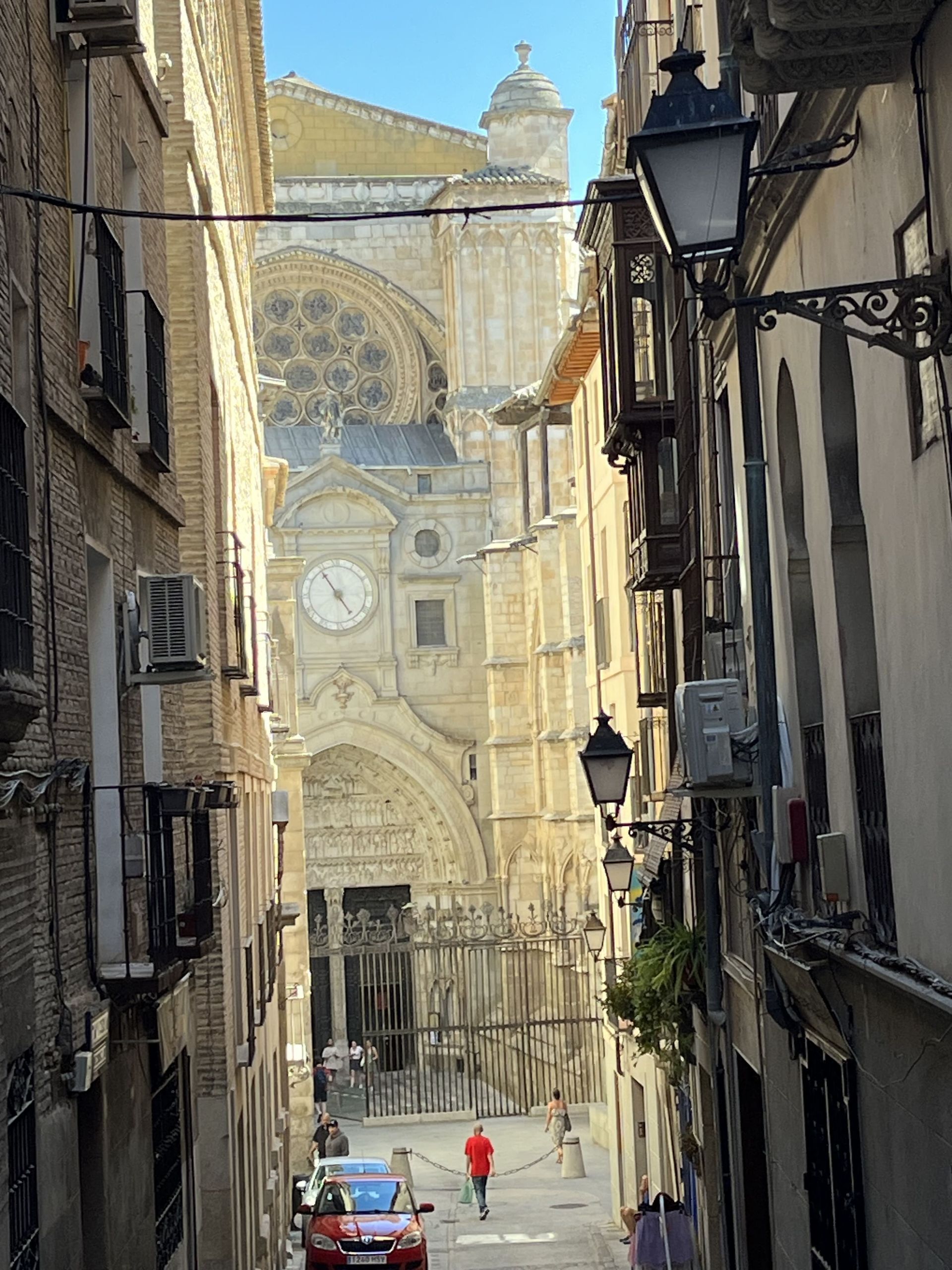 A man in a red shirt is walking down a narrow street in front of a cathedral.
