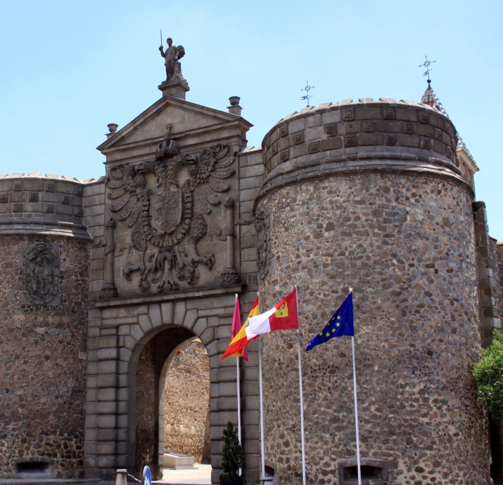 Three flags are flying in front of a stone building