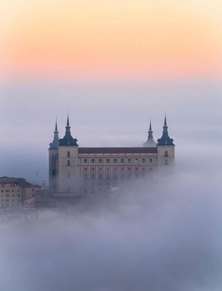 A castle is surrounded by fog at sunset.