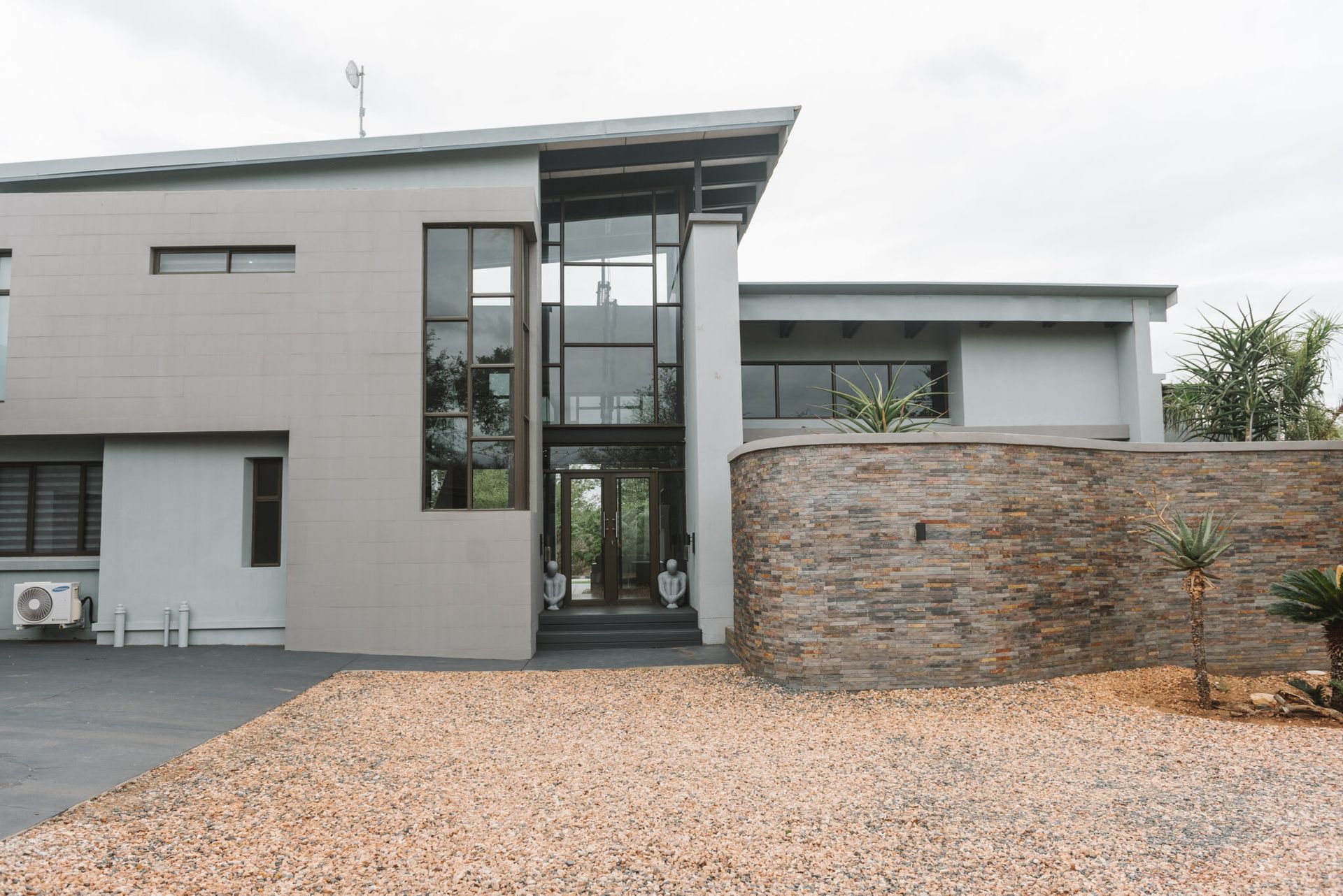 Modern gray building with stone wall and gravel, tall glass entrance.