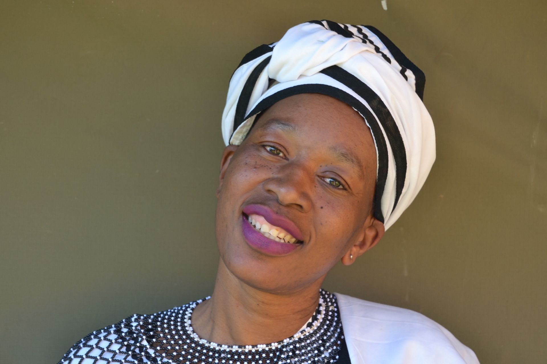 Woman with a black and white headwrap, smiling, against a brown wall.