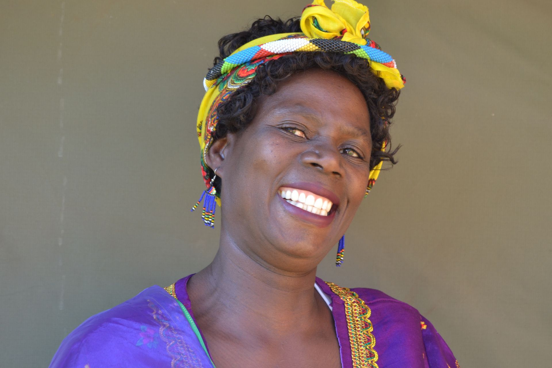 Smiling Black woman wearing a yellow headscarf and purple dress.