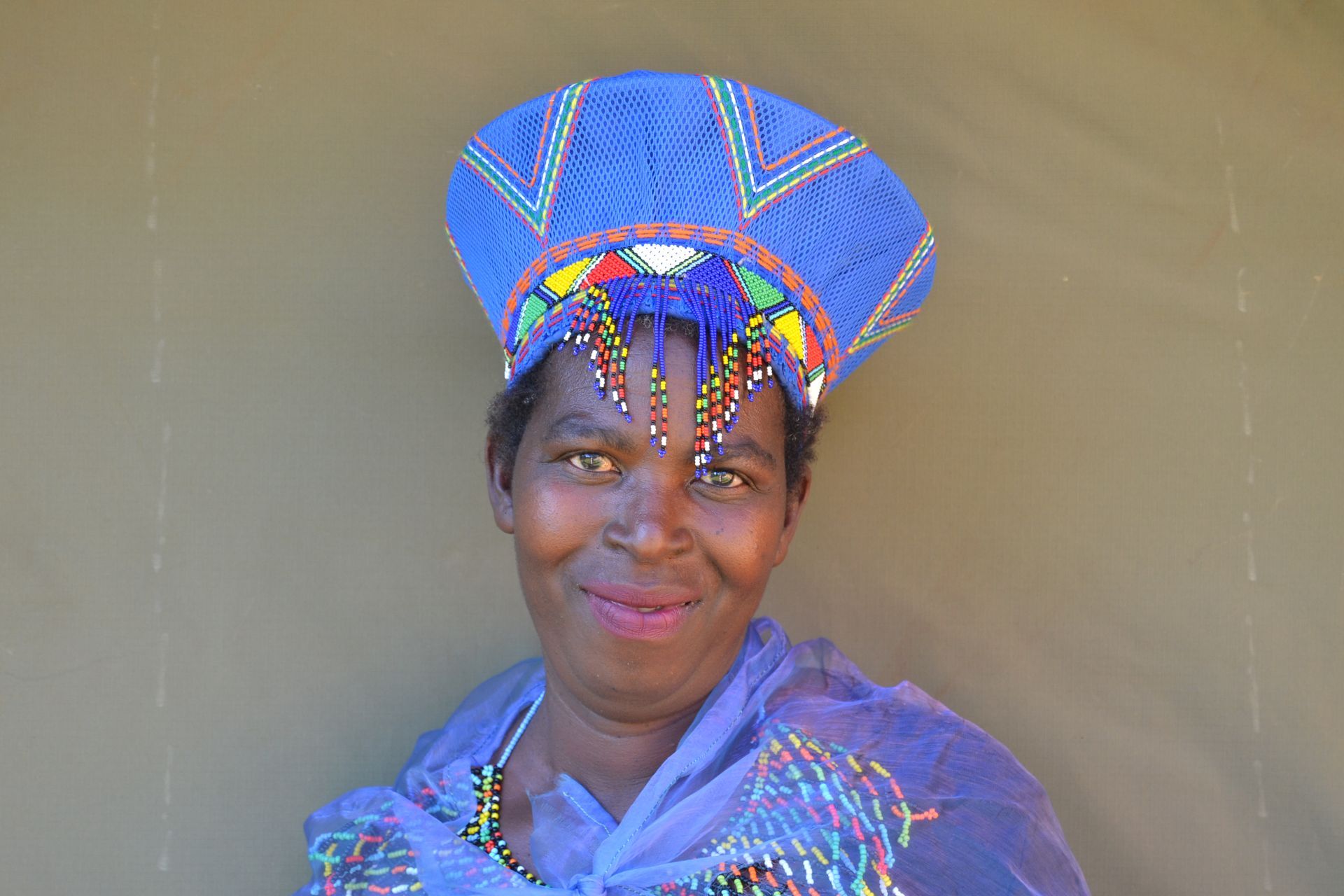 Woman in blue beaded headdress and shawl, smiling.