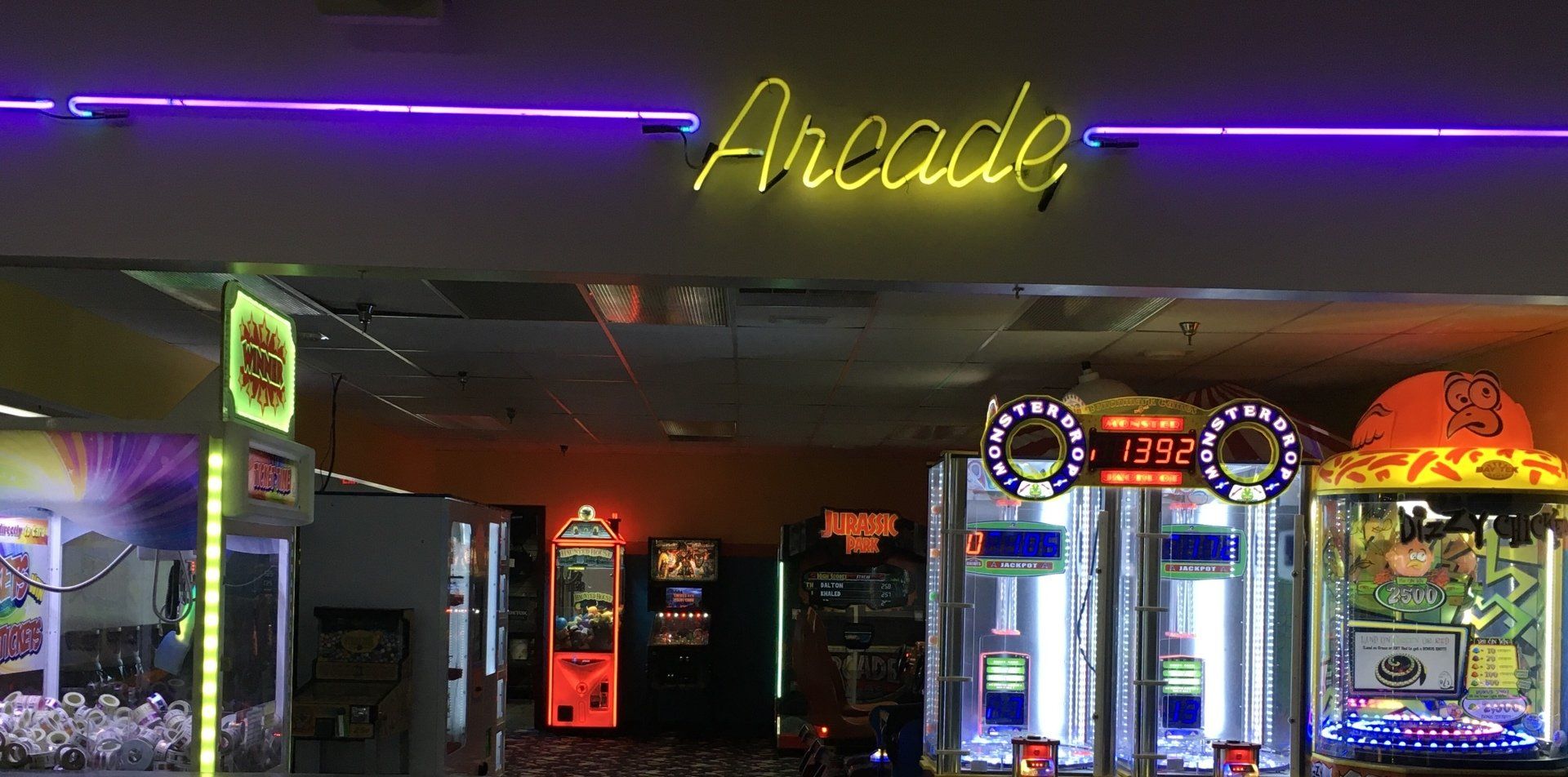 A neon sign that says arcade is hanging from the ceiling of an arcade.
