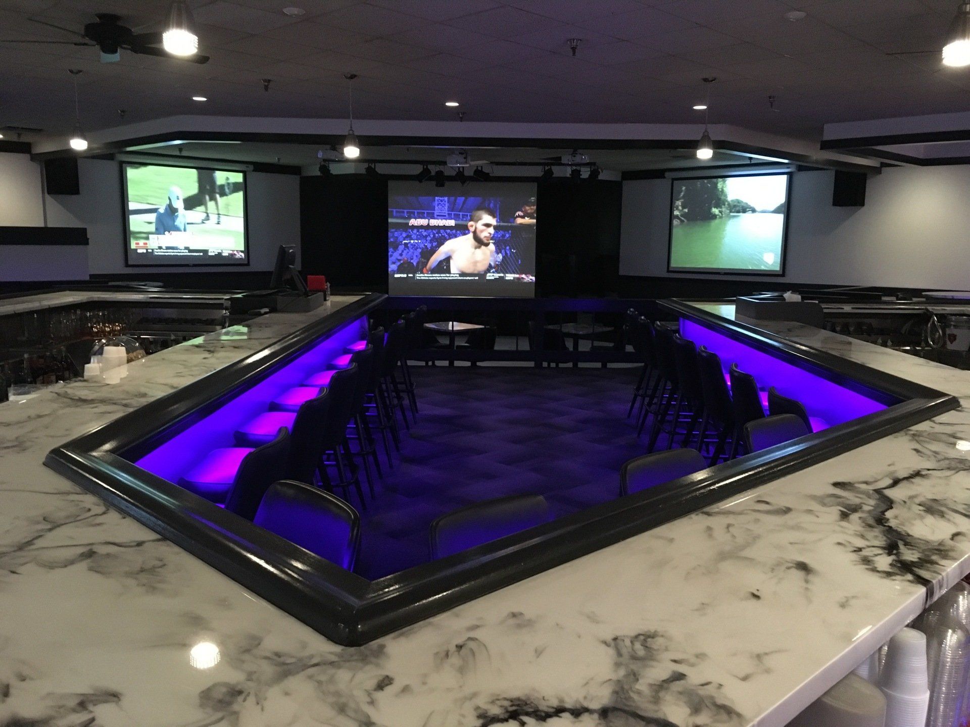 A large room with tables and chairs and a large screen on the wall.