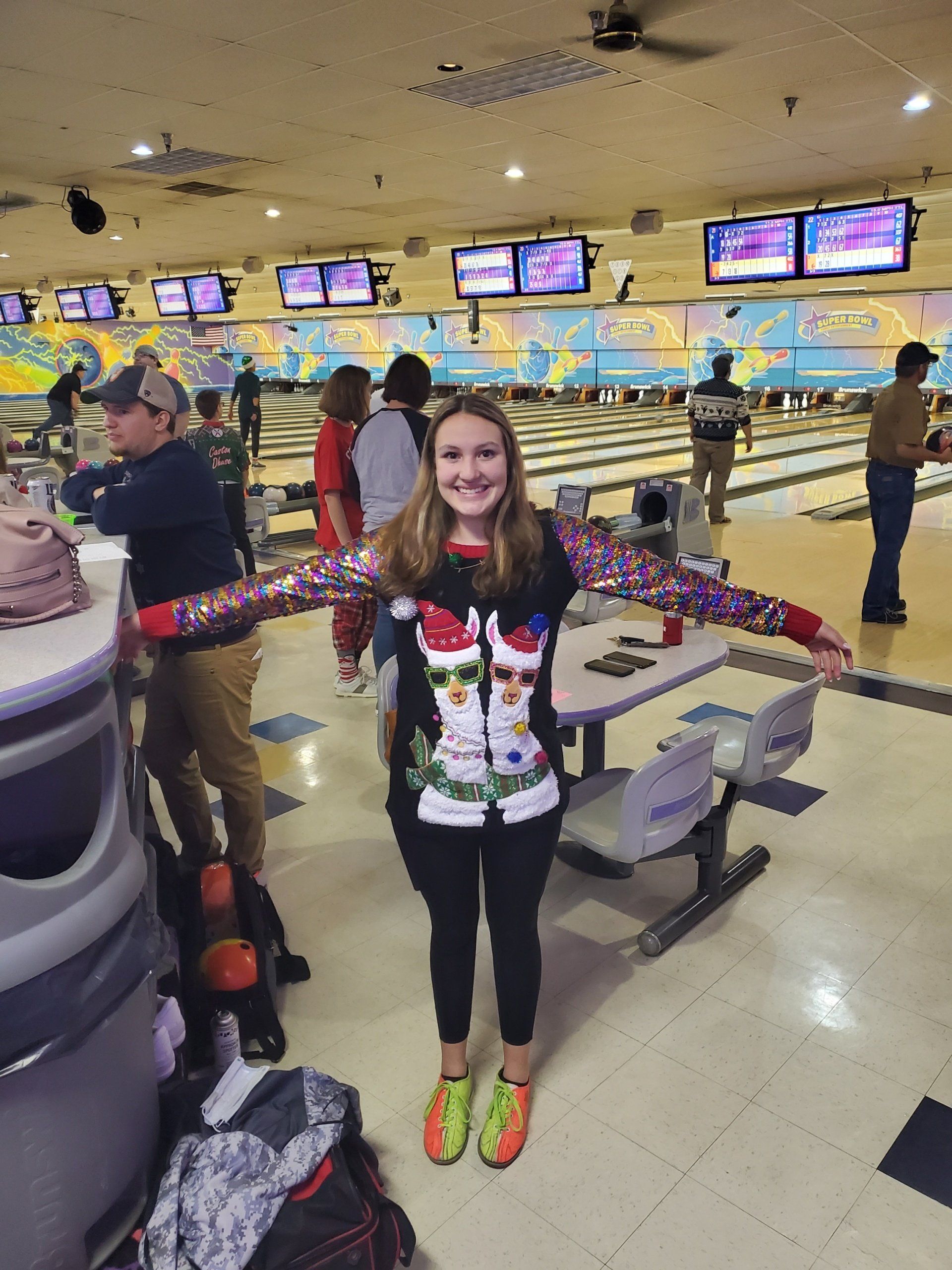 A woman in a christmas sweater is standing in a bowling alley.