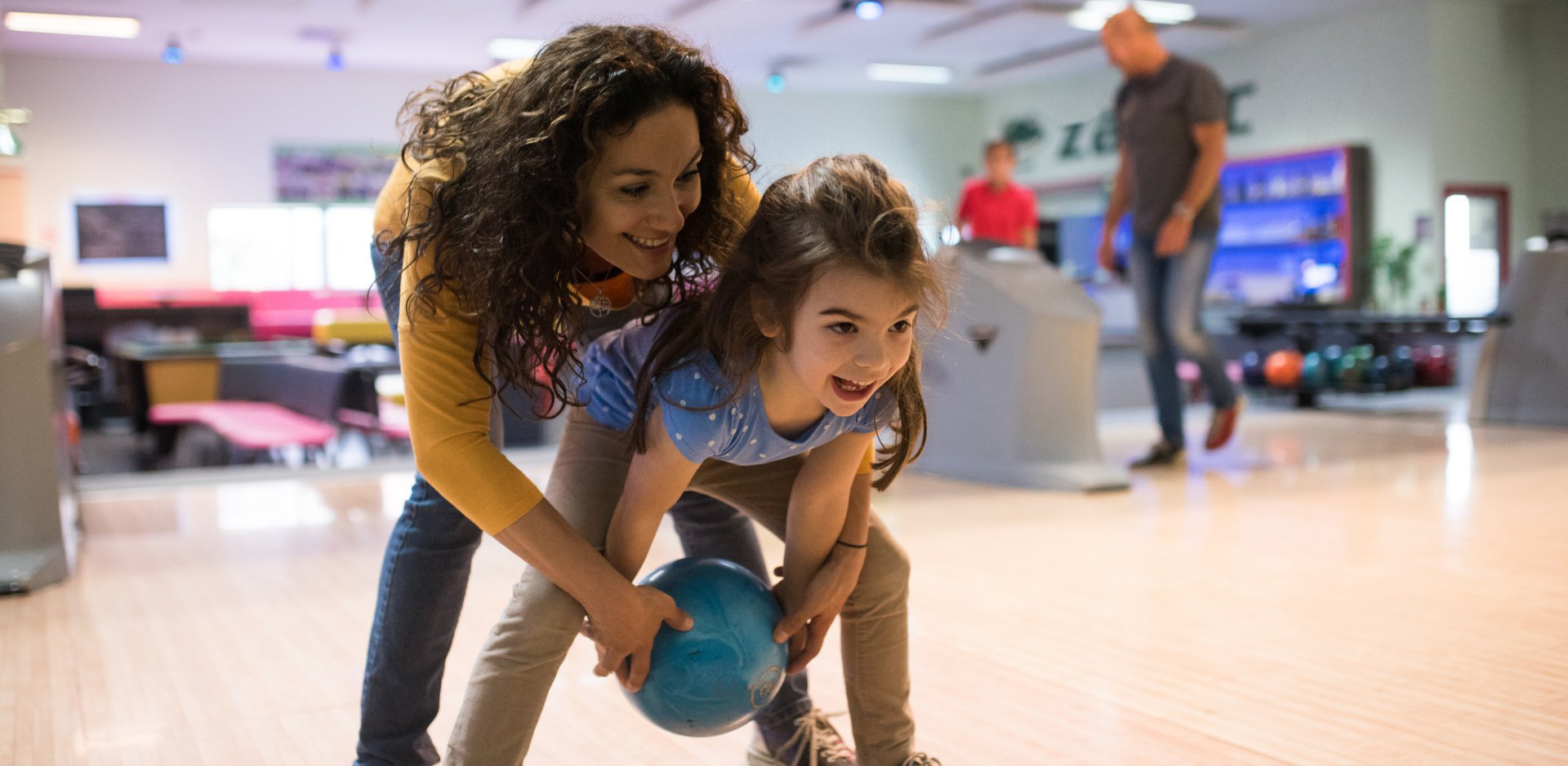 A woman and a little girl are bowling together at a bowling alley.