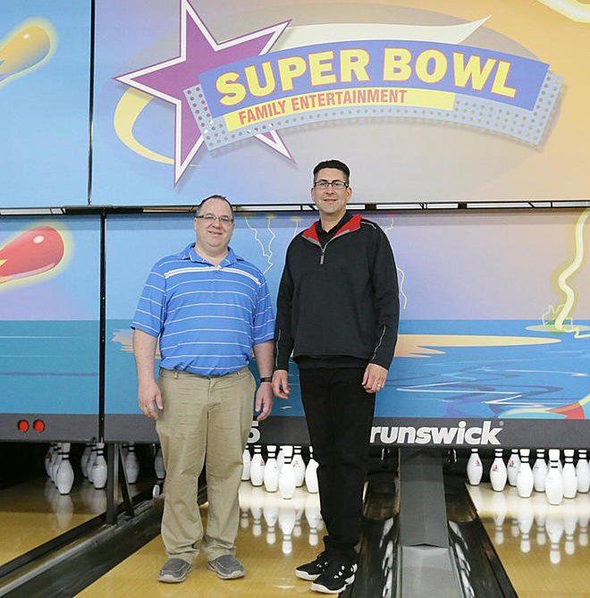 Two men are standing in front of a super bowl sign
