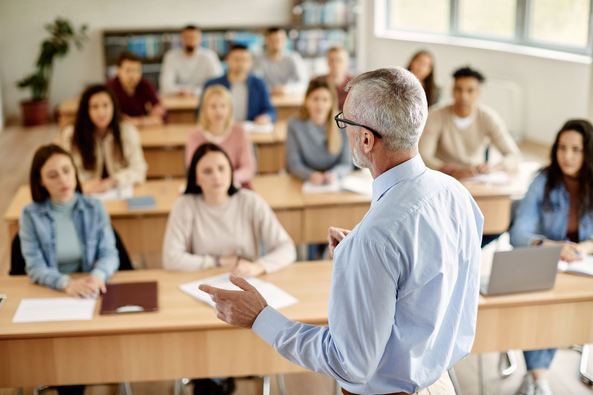 um homem está fazendo uma apresentação para um grupo de alunos em uma sala de aula.
