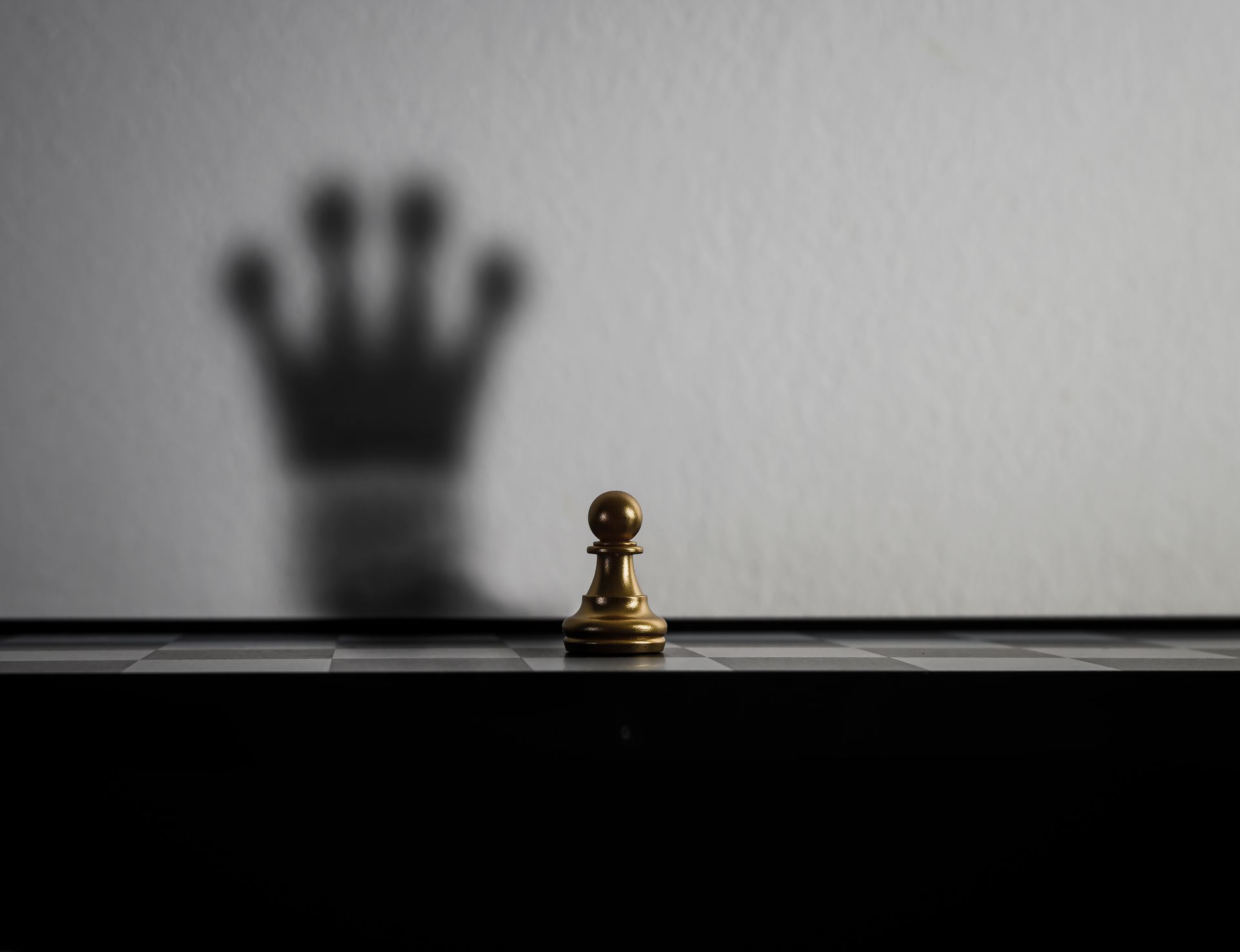 um peão em um tabuleiro de xadrez com a sombra de uma coroa na parede atrás dele.