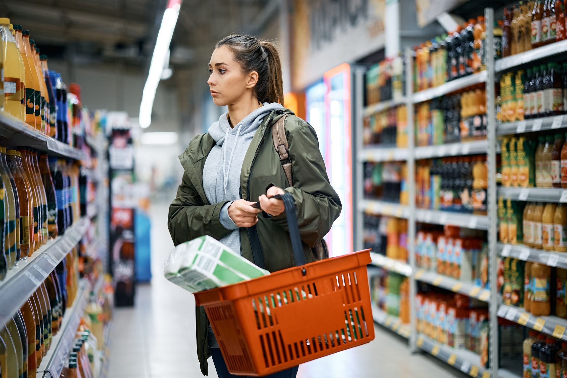 Uma mulher está fazendo compras em um supermercado com uma cesta laranja.





