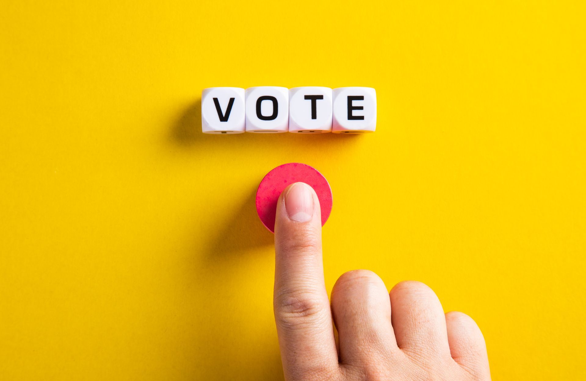 a person is pressing a red button that says vote on a yellow background .