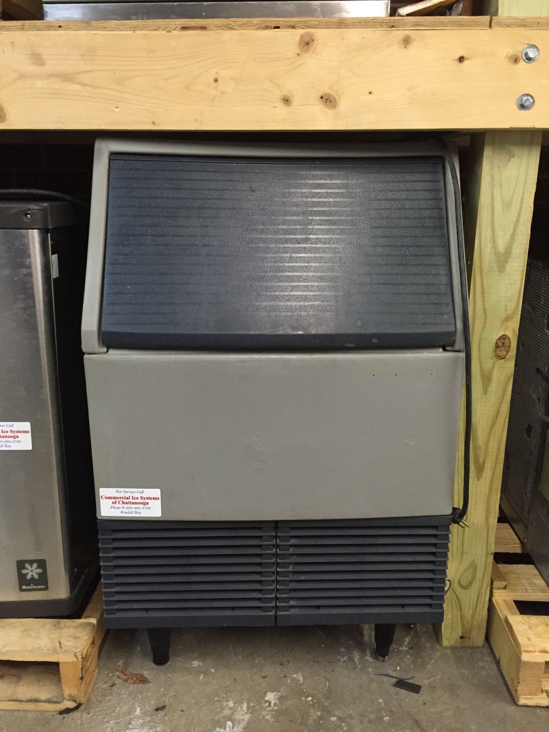An ice machine is sitting under a wooden shelf