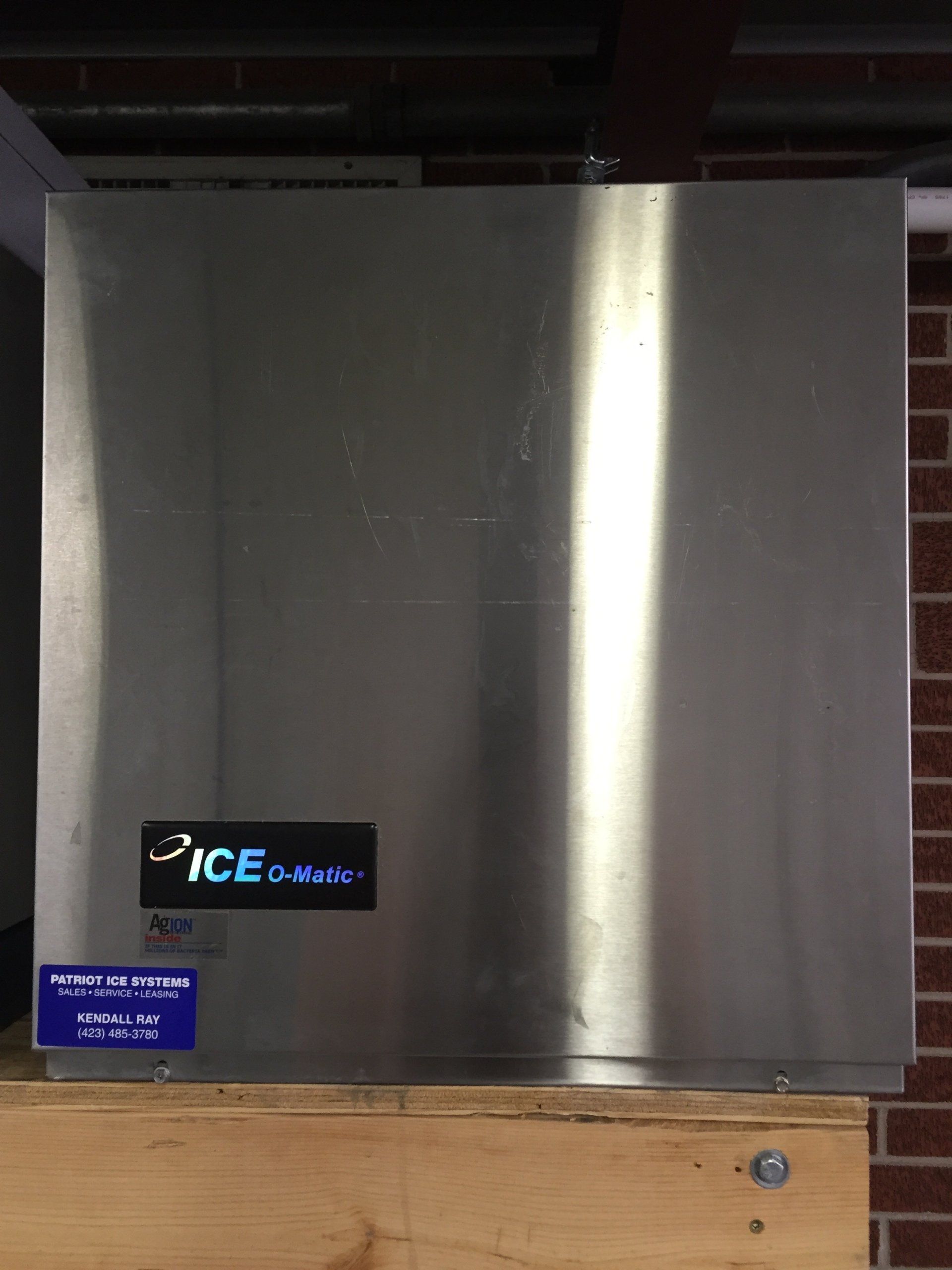A stainless steel ice machine is sitting on a wooden table.