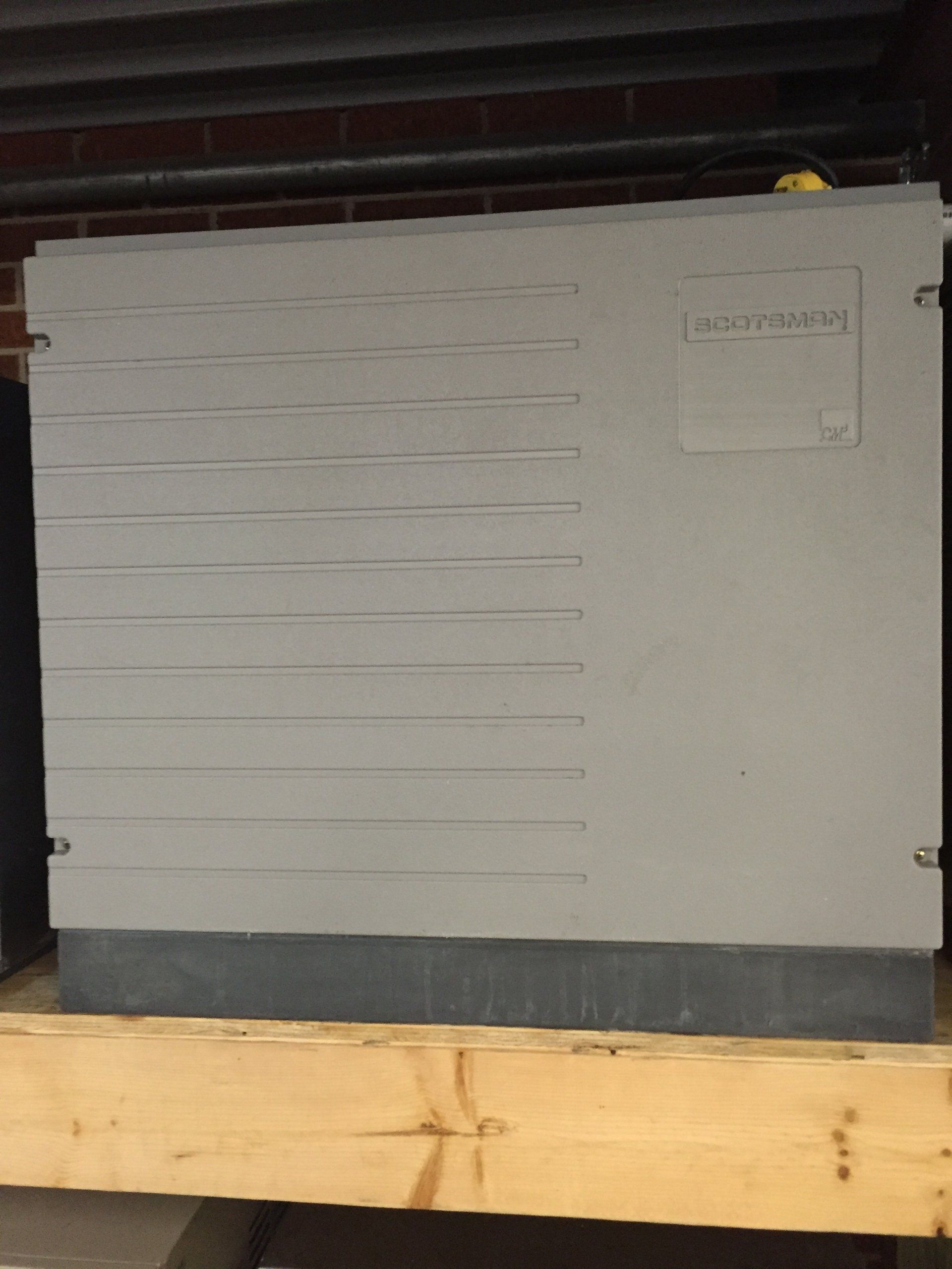 A white ice machine is sitting on top of a wooden shelf.